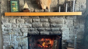 A stone fireplace with a mounted deer head, a framed fish illustration, and a guitar.