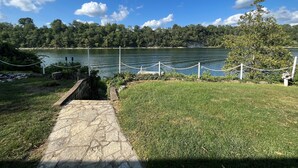 A stone pathway leading to a lake with a rope barrier and a grassy area.