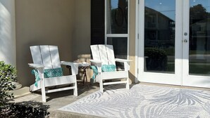 Un patio couvert avec deux chaises blanches et une petite table, une porte vitrée et un tapis à motifs.