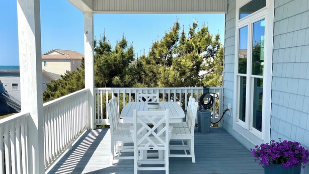 A covered porch with a white table and chairs, a potted plant, and a view of the ocean and trees. - Newer Ocean View home w/Pool.....Walk to Ocean and Intercoastal (Oak Island)