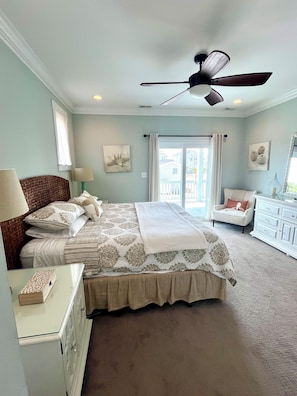 A bedroom with a bed, a ceiling fan, a dresser, a chair, and a view of the outside.