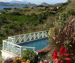 Une piscine ornée d’une balustrade blanche, entourée d’une végétation luxuriante et avec une chaîne de montagnes en toile de fond.
