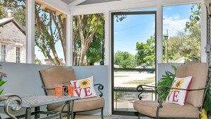 Une véranda avec deux fauteuils rembourrés, une table en métal et une vue sur l’extérieur.