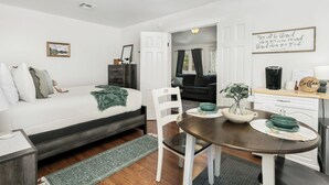 Une pièce compacte et bien éclairée, comprenant un lit, une table à manger avec des chaises, un coin café et donnant sur une autre pièce.