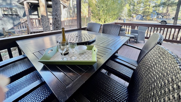 An outdoor patio with a table set for two, featuring a bottle of wine, glasses, and a bowl. - Cozy Cabin in the woods  (Munds Park)