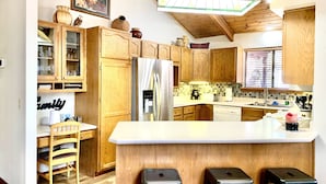A kitchen with wooden cabinets, a stainless steel refrigerator, a white countertop, and a hanging light fixture. - Cozy Cabin in the woods  (Munds Park)