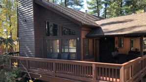 A wooden cabin with a deck, large windows, and a covered outdoor seating area. - Cozy Cabin in the woods  (Munds Park)