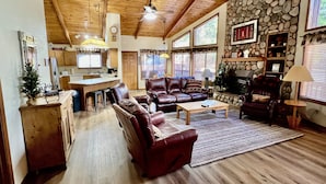 A spacious living room with a fireplace, leather sofas, and a stone wall. - Cozy Cabin in the woods  (Munds Park)