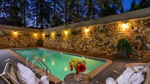 Un espace aménagé au bord de la piscine, avec un mur en pierre, des chaises longues et une petite table sur laquelle est posé un vase de fleurs.