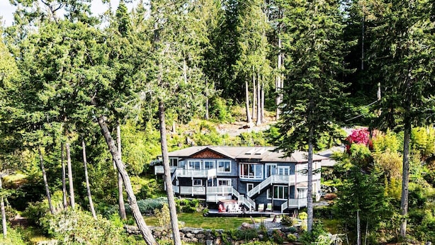 Ein zweistöckiges Haus mit Balkon, umgeben von dichtem Wald und einer felsigen Küstenlinie.