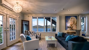 Ein geräumiges Wohnzimmer mit großen Fenstern und Blick auf eine Brücke und Hügel. Es gibt zwei Sessel, ein Sofa und einen Couchtisch.