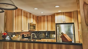 Uma cozinha com armários de madeira, micro-ondas, geladeira de aço inoxidável, cafeteira e porta-facas.