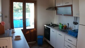 Eine kompakte Küche mit Herd, Spüle und Schränken. Ein Fenster sorgt für natürliches Licht und einen Ausblick nach draußen.