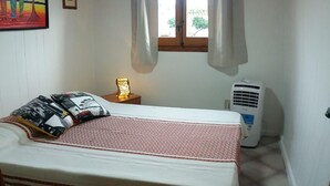 Ein Schlafzimmer mit einem Bett, einem Nachttisch mit Lampe, einem Fenster mit Vorhängen und einer Klimaanlage.