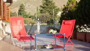 Eine Terrasse mit zwei roten Stühlen und einem kleinen Tisch, auf dem sich eine Flasche und eine Schüssel befinden.