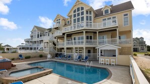 A multi-story hotel with a swimming pool, outdoor seating, and a hot tub. - Premier Oceanfront Dog Friendly w/ Pool, Hot Tub, Elevator, Game & Theater Rooms (Avon)