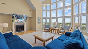 A spacious living room with a fireplace, large windows, and a view of the outside. - Premier Oceanfront Dog Friendly w/ Pool, Hot Tub, Elevator, Game & Theater Rooms (Avon)
