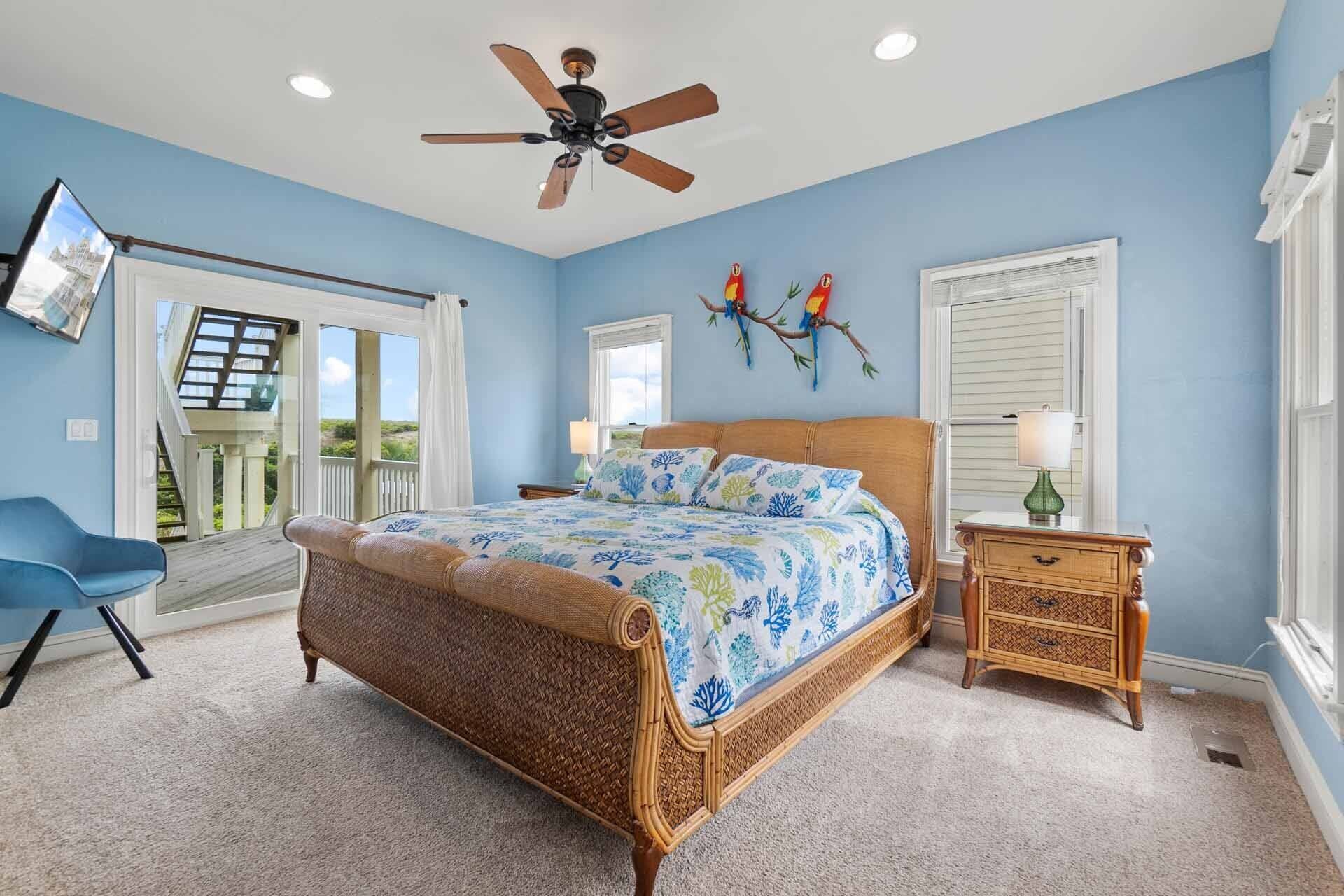 Un dormitorio con cama, ventilador de techo, mesita de noche, una silla y ventana con contraventanas.