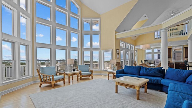 A spacious living room with large windows, a blue sofa, wicker chairs, and a white coffee table. - Premier Oceanfront Dog Friendly w/ Pool, Hot Tub, Elevator, Game & Theater Rooms (Avon)