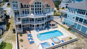 A multi-story hotel with a large swimming pool, outdoor seating, and a covered area with lounge chairs. - Premier Oceanfront Dog Friendly w/ Pool, Hot Tub, Elevator, Game & Theater Rooms (Avon)
