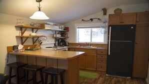 Een keuken met houten kastjes, een zwarte koelkast, een houten kookeiland met barkrukken, en een raam dat natuurlijk licht binnenlaat.