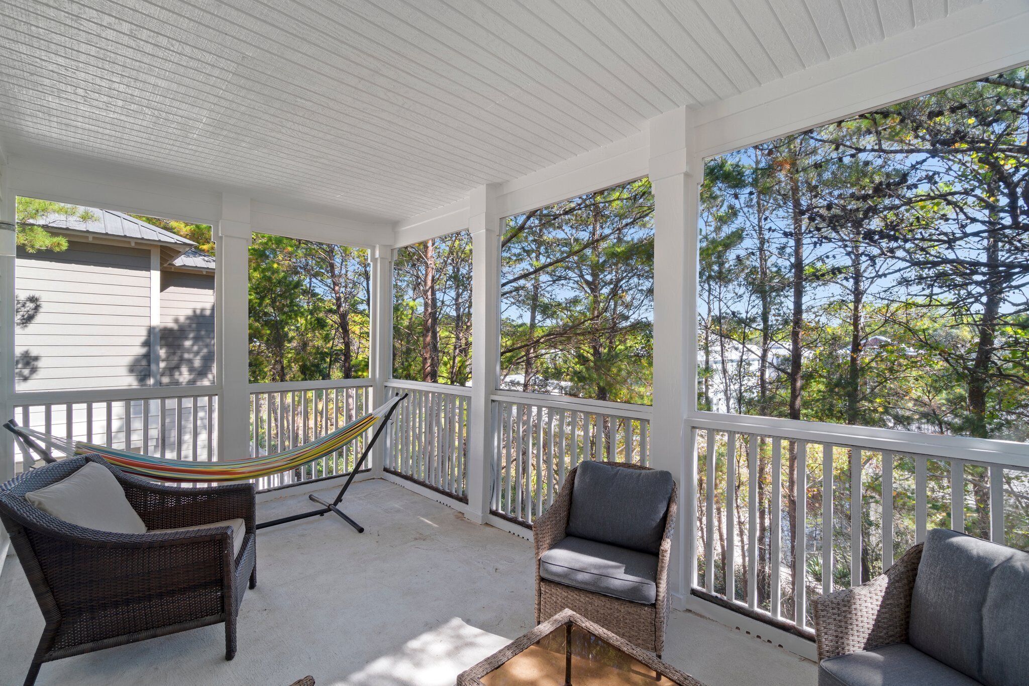 A covered porch with wicker furniture, a hammock, and a view of trees.