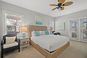 A bedroom with a large bed, a wicker headboard, a ceiling fan, and a nightstand with a lamp.