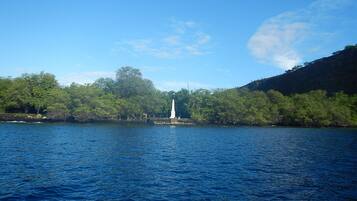 A calm lake with a white monument in the center, surrounded by lush greenery and a clear blue sky.