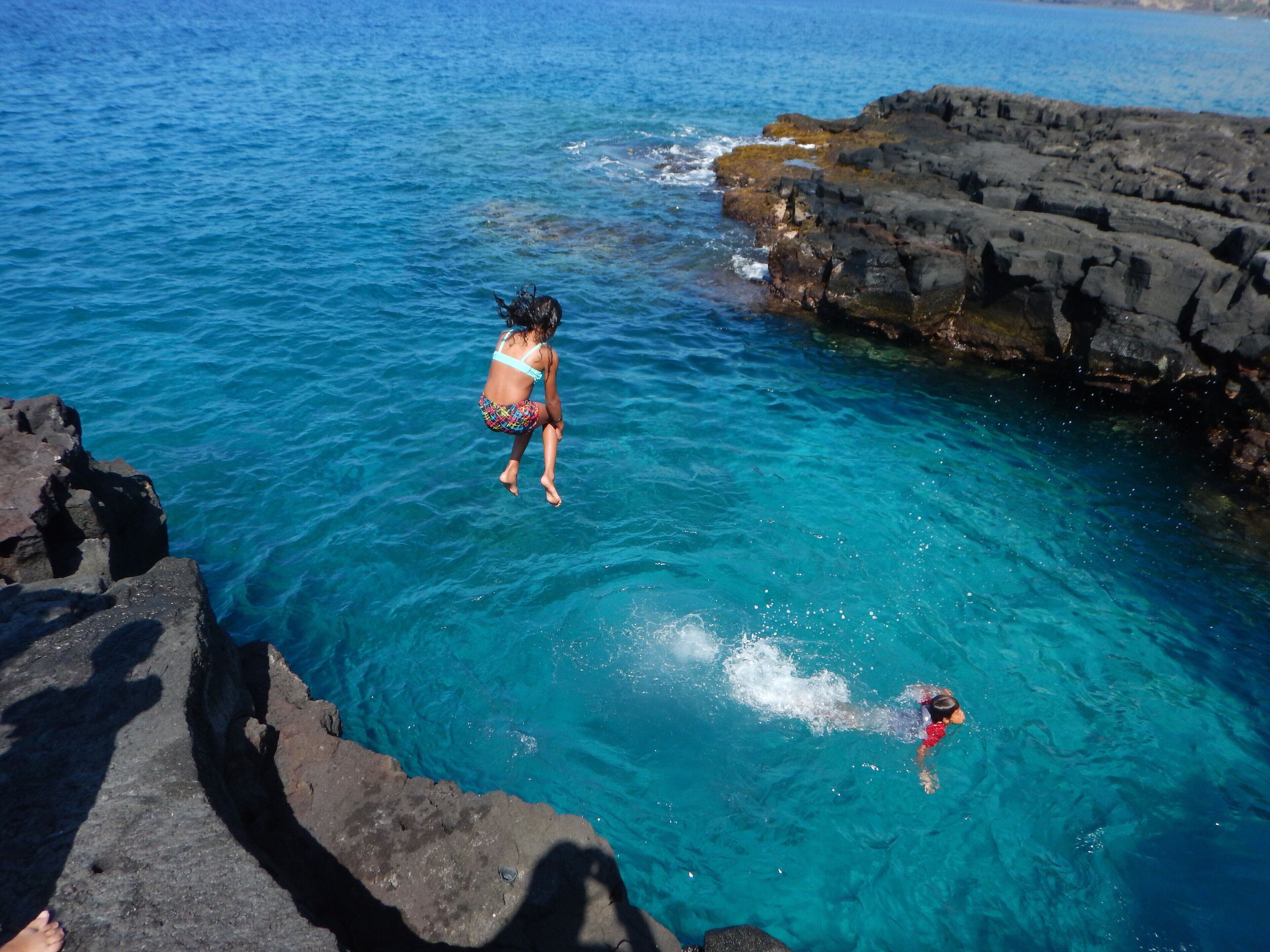 A person jumping into clear blue water near rocky cliffs.