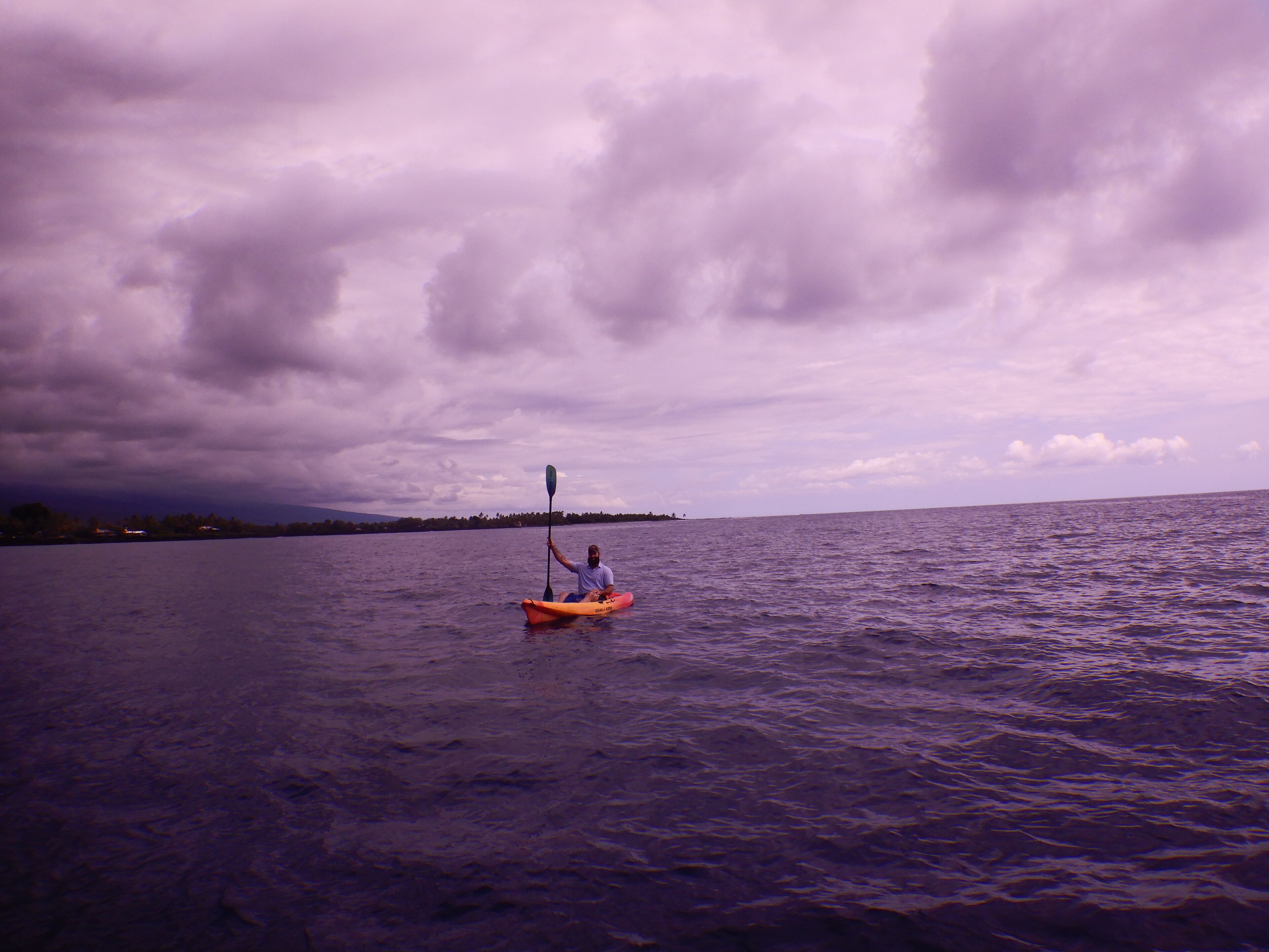A person kayaking on a calm body of water with a cloudy sky.