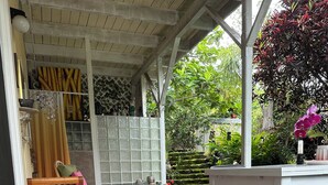 A covered patio area with a stone floor, wooden furniture, and a table with a candle. - Sweet Mermaid Studio at Manini Beach, Kealakekua Bay (Captain Cook)