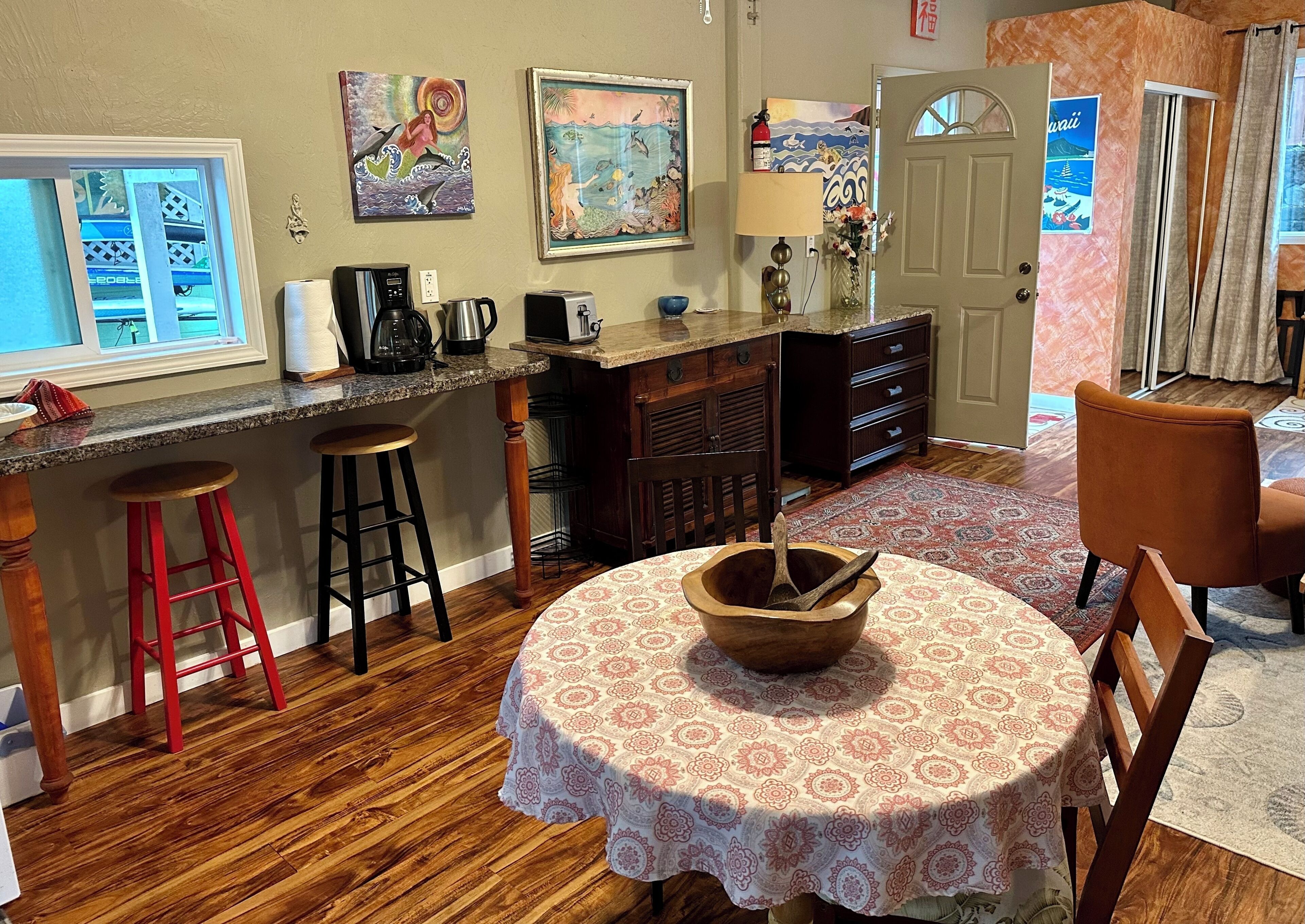 Una cocina con una isla de madera, taburetes de bar, una mesa de comedor con mantel estampado y obras de arte en las paredes.