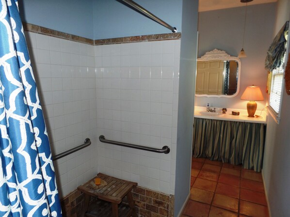A bathroom with a shower, a small wooden stool, a sink with a mirror, and a lamp.