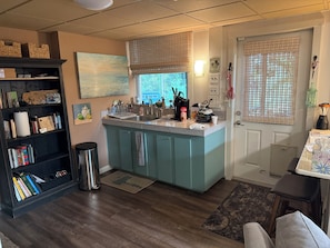 A kitchen with a central island, wooden cabinets, a bookshelf, and a dining area with a table and chairs.