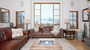 A cozy living room with a brown leather sofa, a wooden coffee table, and a view of mountains through large windows. - Big Sky Vacation Rentals: MMH 5 Derringer (Big Sky)
