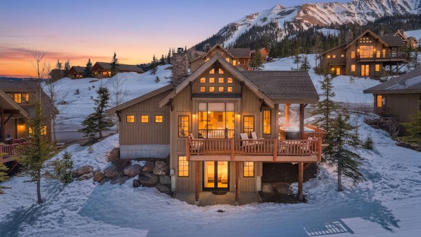 A lodge with a large deck, multiple windows, and a view of snow-covered mountains. - Big Sky Vacation Rentals: MMH 5 Derringer (Big Sky)