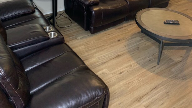 Ein Wohnzimmer mit einem braunen Ledersofa, einem runden Couchtisch, einem Beistelltisch mit Lampe, einem Deckenventilator und einem Stadtbild an der Wand.