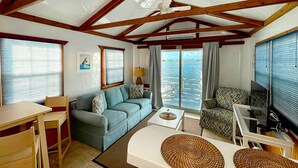 Una sala de estar con sofá, sillón y mesa de centro, televisor y balcón con vista al mar.