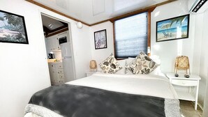 Un dormitorio con cama, mesita de noche, ventana con persianas y puerta que da a un baño.