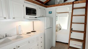 Una cocina compacta con armarios blancos, microondas, estufa y refrigerador.