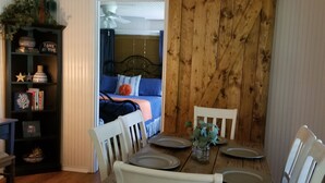A dining area with a wooden table, white chairs, and a ceiling fan. A bookshelf with decorative items is visible to the left. - HIDEAWAY at HAWKINS!East TX LAKEFRONT Cabin in the Trees-Firepit-Private dock🐟 (Hawkins)