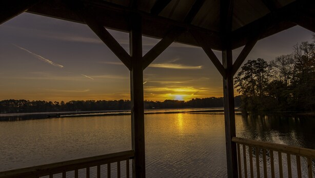 A wooden deck with a view of a sunset over a calm lake. - HIDEAWAY at HAWKINS!East TX LAKEFRONT Cabin in the Trees-Firepit-Private dock🐟 (Hawkins)