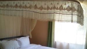 A bed with white linens, a headboard, and a window with curtains. - Forest Breeze Gardens (Nairobi)