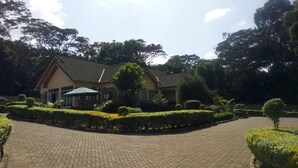 A building with a brick pathway leading to it, surrounded by well-maintained hedges and trees. - Forest Breeze Gardens (Nairobi)