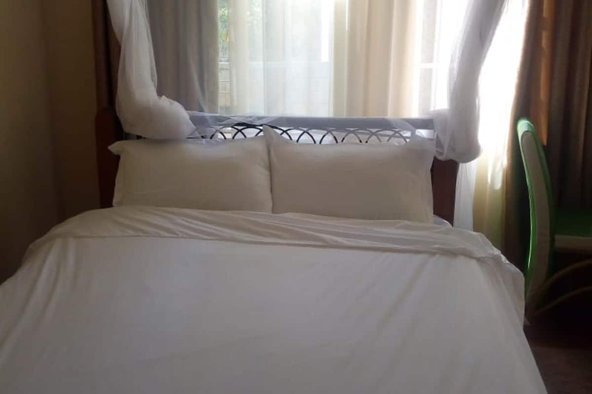 A bed with white bedding and a canopy, a window with sheer curtains, and a green chair.