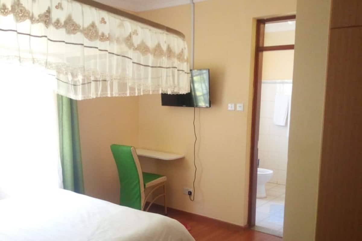 A hotel room with a bed, a desk, a chair, a television, and a bathroom visible through an open door.