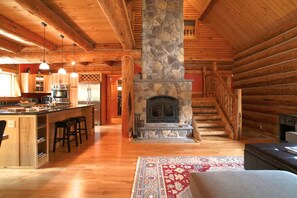 A log cabin interior with a stone fireplace, wooden beams, a kitchen with bar stools, and a staircase. - Stunning Private Lodge, Sauna  (Wilmington)