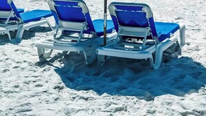 Una playa con tres tumbonas azules bajo un parasol azul.