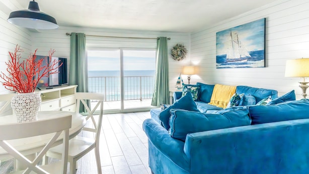 Una habitación con un sofá azul, una mesa blanca y vistas al océano.