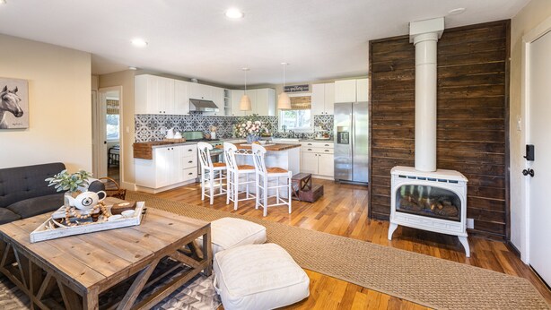 A modern kitchen with white cabinets, a central island, and a wood-burning stove. - The B’s Hive Cottage (Newbury Park)